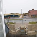 Balcony with two wicker chairs and table overlooking street and houses.