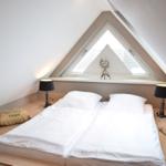 Schlafzimmer mit Dachschrägen, Doppelbett, zwei Nachttischen und einem Dreiecksfenster.