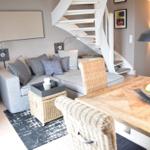 Wohn- und Essbereich mit grauem Sofa, Holztisch und Wendeltreppe.