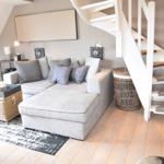 Wohnzimmer mit grauem Sofa, Holzboden und Wendeltreppe.