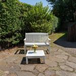 Weiße Bank und Tisch mit Blumen auf Steinplatten im Garten.