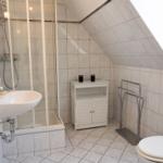 Badezimmer mit Dusche, Waschbecken und Toilette unter schräger Decke.