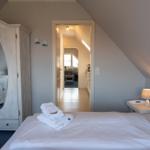 Schlafzimmer mit Dachschräge, weißem Bett und Kleiderschrank mit Spiegel.