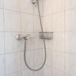 Dusche mit Handbrause und Duschgitter an weißen Fliesen