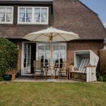 House with garden, umbrella, loungers, and flowerbeds.