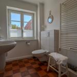 Bathroom with sink, toilet, and window. Terracotta floor and radiator.