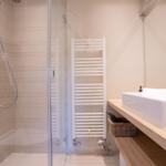 Dusche mit Glaswand, Handbrause und Heizkörper neben Waschbecken.