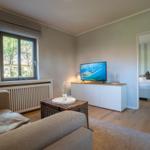 Wohnzimmer mit Sofa, Fernseher und Blick auf Schlafzimmer.
