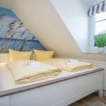 Bedroom with sloped ceiling, bed with yellow pillows, and wall mural of beach.