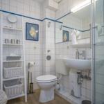 Bathroom with shower, sink, and toilet. White tiles and blue accents.