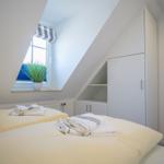 Bedroom with sloped ceiling, bed, and wardrobe. Window with plant and striped roller blind.