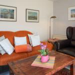 A living room with orange sofa, brown armchair, and wooden table with flowers.