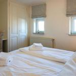 Bedroom with bed, wardrobes, and windows with roller blinds.