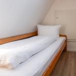 A bed with white bedding and wooden frame under a sloped ceiling.