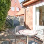 Terrace with table and two chairs in front of a house wall.