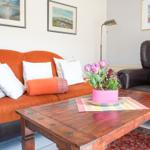 A living room with orange sofa, brown armchair, and wooden table with flowers.