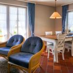 Two blue chairs and a dining table with chairs in the room with windows and terrace.