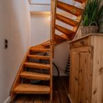 Holztreppe führt zur oberen Etage. Holzschrank und Pflanze im Vordergrund.