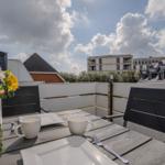 Terrasse mit Tisch, Stühlen und Blumen. Blick auf Gebäude und Himmel.