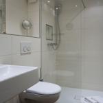 Badezimmer mit Dusche, Waschbecken und Toilette. Weiße Fliesen und moderne Armaturen.