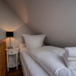 Ein Bett mit weißer Bettwäsche und Handtüchern. Neben dem Bett steht ein Nachttisch mit einer Lampe.