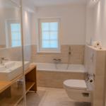 Badezimmer mit Badewanne, Toilette und Waschbecken auf Holzuntergestell.