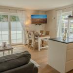 Küche und Esszimmer mit Holzboden und Fenstern. Esstisch mit Stühlen und Fernseher an der Wand.