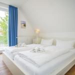 Schlafzimmer mit Doppelbett, Fenster und Holzboden.