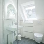 Badezimmer mit Dusche, Waschbecken und Toilette unter Dachschrägen.