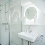 Badezimmer mit Dusche, Waschbecken und runden Spiegel