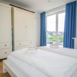 Zimmer mit Doppelbett, weißen Schränken und blauen Vorhängen vor Fenster