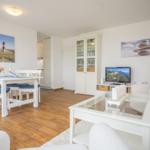 Wohnzimmer mit Esstisch, Fernseher und Glas-Tisch. Hölzerner Boden und weiße Möbel.