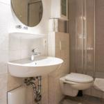 Badezimmer mit Waschbecken, Spiegel, Toilette und Dusche.