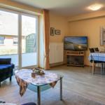Wohn- und Essbereich mit TV, Tisch und Stühlen, großes Fenster und Wandbild mit Möwe.