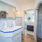 Badezimmer mit Waschbecken, Spiegel und Dusche. Blick in Schlafzimmer mit Bett.