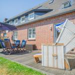 Terrasse mit Tisch, Stühlen und Sonnenschirm. Weiße Strandkörbe stehen auf der Terrasse.