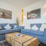 Zwei blaue Sofas mit Kissen stehen um einen Holztisch herum. An den Wänden hängen Bilder.