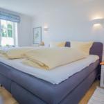 Schlafzimmer mit Bett, Nachttisch und Fenster. Decke und Kissen sind gelb.