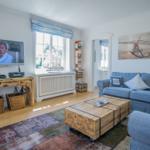 Ein Wohnzimmer mit Sofa, Fernseher und Holztisch. An der Wand hängt ein Bild mit Anker.