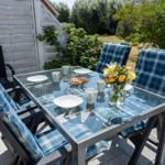 Glas-Tisch mit blauen Kissen und Blumen auf Terrasse
