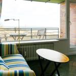 Sofa and table in front of window with view of balcony and sea.