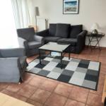 Wohnzimmer mit Sofa, Sessel, Couchtisch und Teppich auf Fliesenboden.