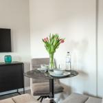 Dining table with chairs, flowers, and water bottle. TV and sideboard in background.
