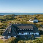 House with thatched roof, surrounded by dunes and sea.