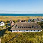 Thatched-roof house surrounded by greenery with a view of the sea.