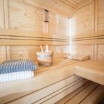 Sauna mit Holzbänken, Handtuch und Eimer.