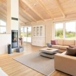 Wohnzimmer mit Holzdecke, Kamin und großem Sofa. Fenster bieten Blick auf die Landschaft.