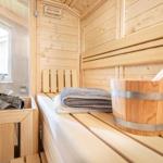 Sauna mit Holzbänken, Eimer und Handtuch. Fenster zur Außenseite.