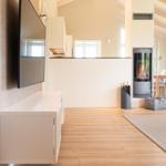 Wohnzimmer mit Kamin, Fernseher und Essbereich. Holzboden und große Fenster.