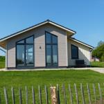 Moderne Holzhütte mit großen Fenstern und Garten. Holzpalisadenzaun im Vordergrund.